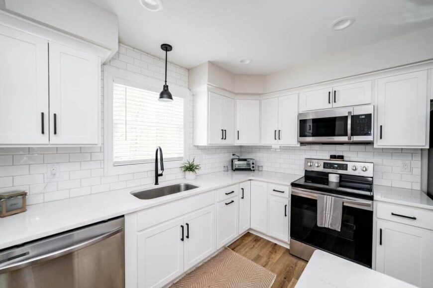 The kitchen has a white subway tile backsplash, matching cabinets, stainless steel appliances, and an undermount sink under a picture window.