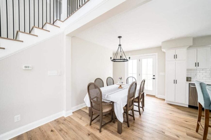 The dining area has round-back chairs and a rectangular table well-lit by a wrought iron chandelier.