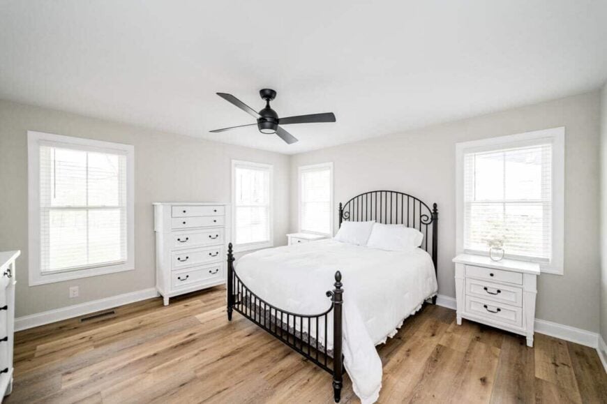 The primary bedroom has white cabinets and an ornate metal bed over the hardwood flooring.