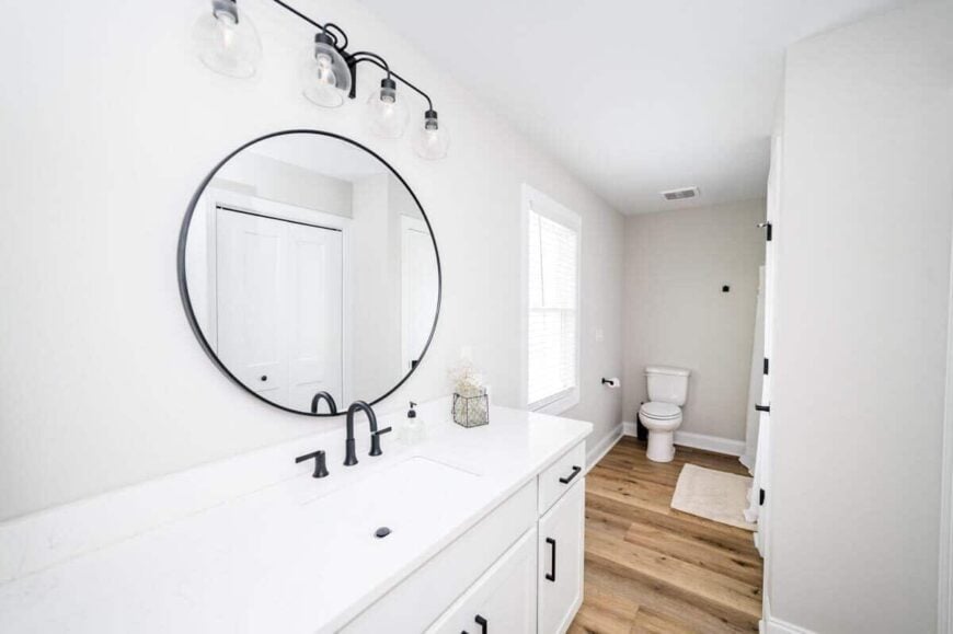 Primary bathroom with a toilet area and a white vanity topped with a round mirror and glass sconces.