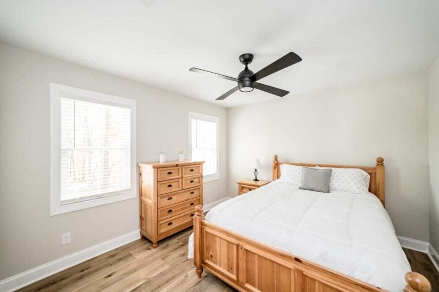 This bedroom has wooden furnishings and a wrought iron fan mounted on the regular ceiling.