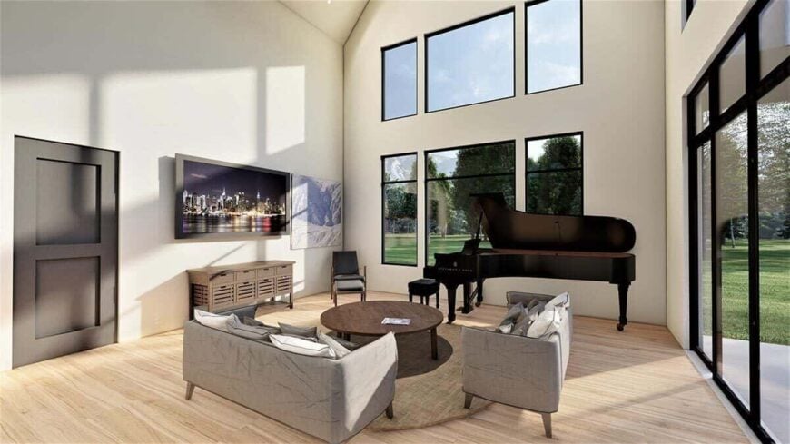 The great room has a two-story ceiling, gray sofas, a grand piano, and massive windows that take in magnificent views and ample natural light.