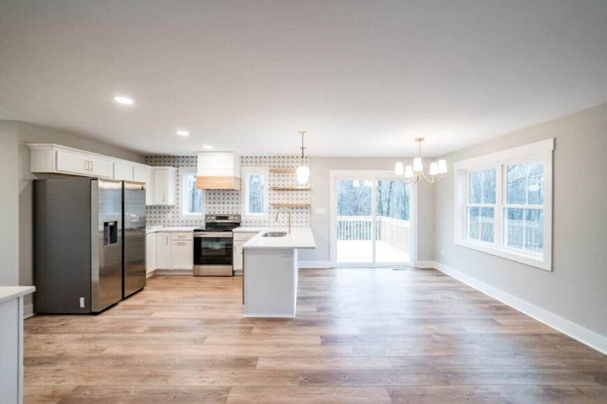 The kitchen and dining space are brightened by brass pendants and white framed windows. Sliding glass doors at the back open to the deck.