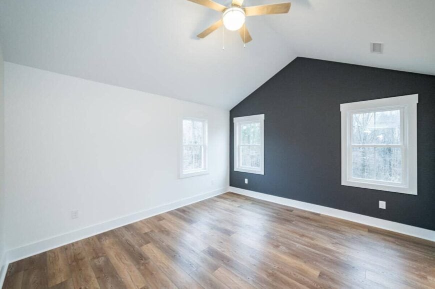 Primary bedroom with a cathedral ceiling, wide plank flooring, and a black accent wall.