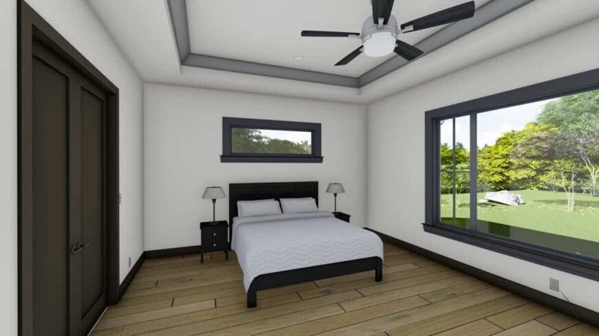 Primary bedroom with a tray ceiling, wide plank flooring, and large windows that frame the lush backyard.