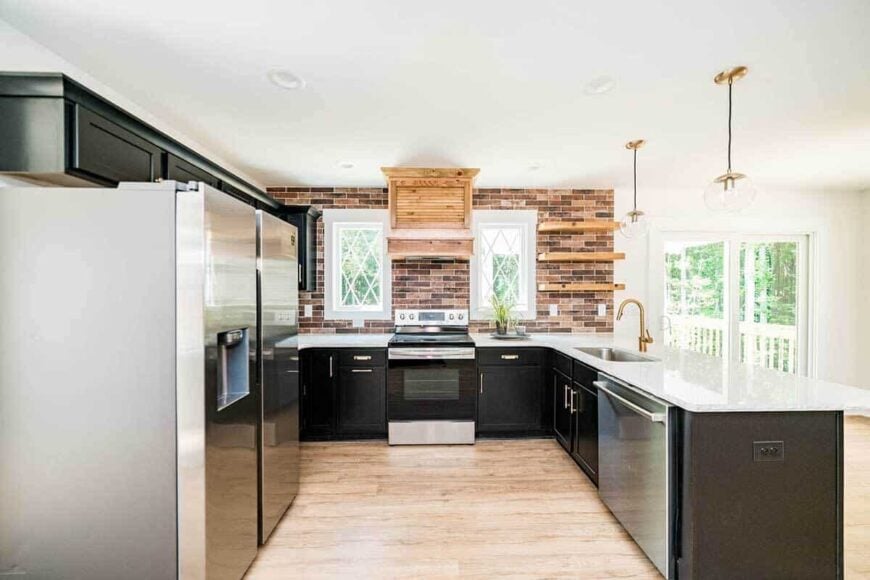 The kitchen has black cabinets, stainless steel appliances, and linear mosaic tiles mounted with floating shelves.
