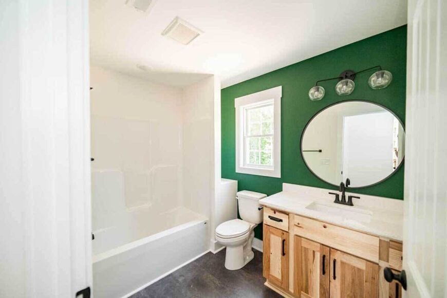 A round mirror and glass sconces mounted against the green wall adorn this bathroom.