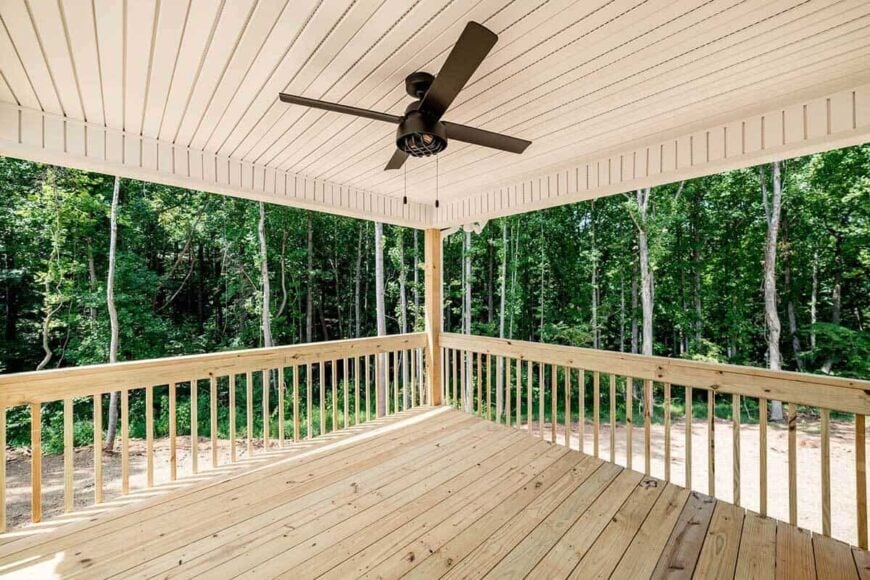 Covered deck with a wrought iron ceiling fan and wooden railings overlooking the lush forest.