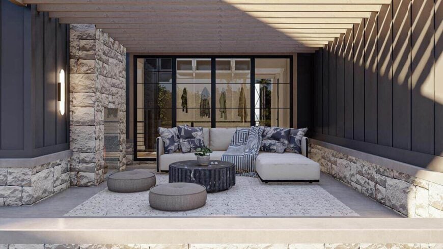 The porch has a trellis roof, a brick fireplace, an L-shaped sofa, and round ottomans sitting on a patterned rug.