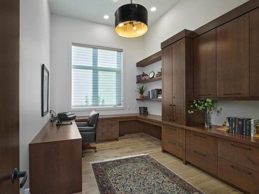 Home office with built-in cabinets, wraparound desks, and a tasseled rug that lays on the hardwood floor.