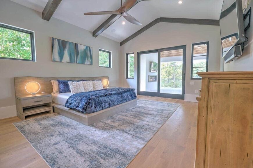 The primary bedroom features a bespoke wooden bed, a cathedral ceiling with exposed beams, and private porch access via sliding glass doors.