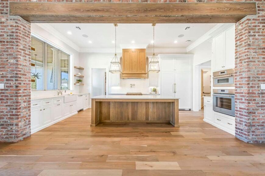 Brick pillars highlight the kitchen. It is equipped with stainless steel appliances, white cabinetry, and a center island that blends in with the hardwood floor.