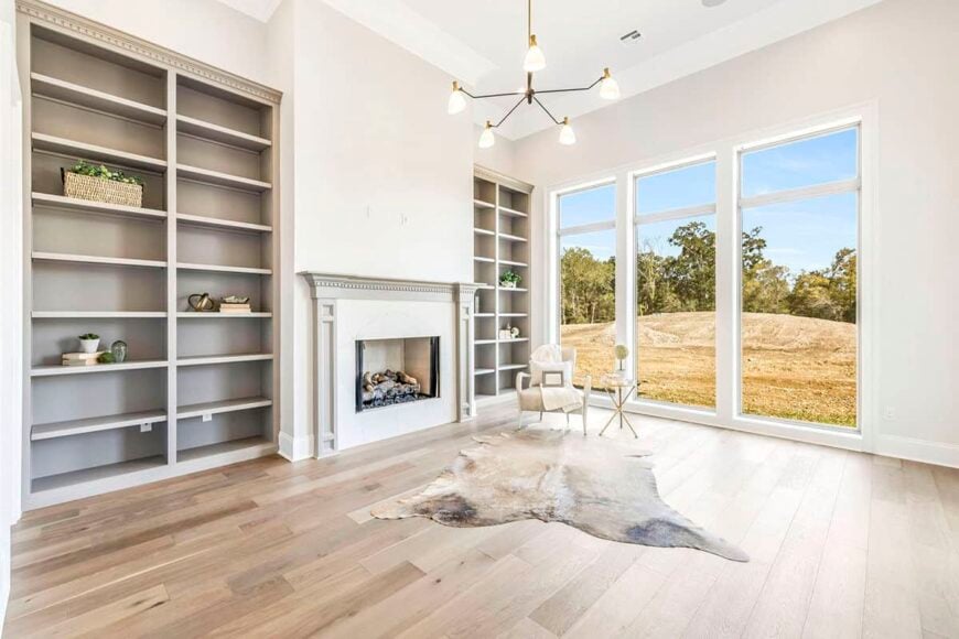 Game room with tall windows, built-in shelves, a fireplace, and a contemporary armchair that sits on a cowhide rug.