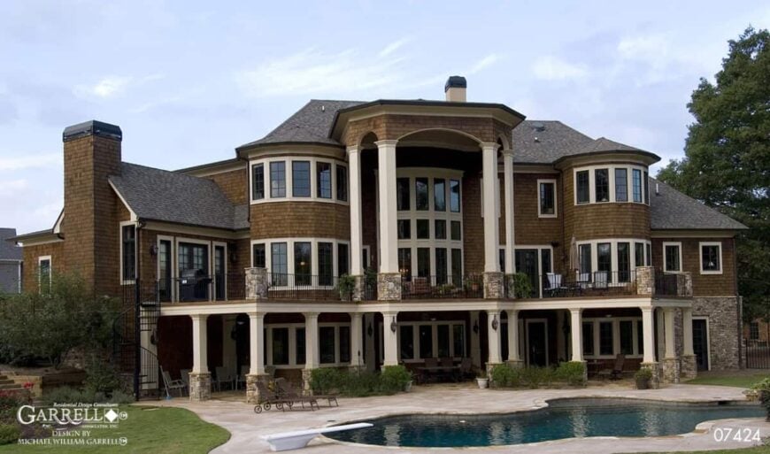 Rear exterior view showcasing the expansive porches, pool terrace, and a multitude of large windows.