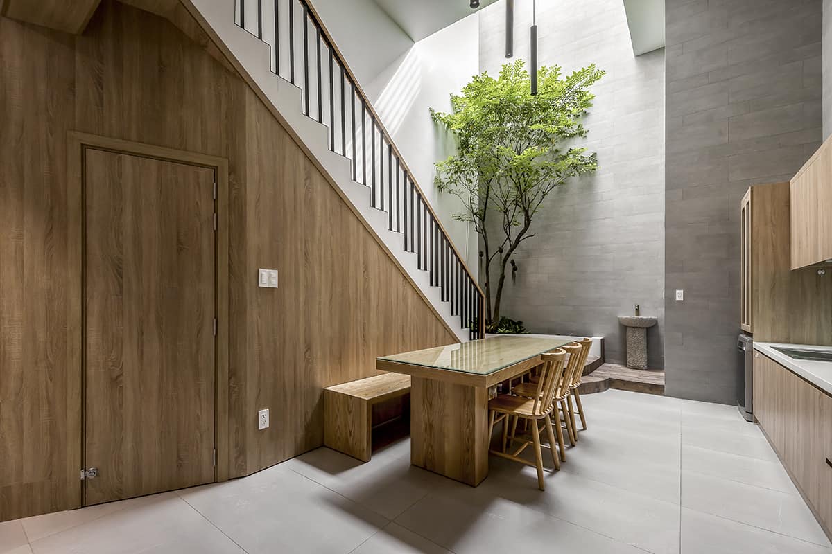 The dining area is situated against the staircase. It is brightened by an atrium that features a lovely tree in the corner.