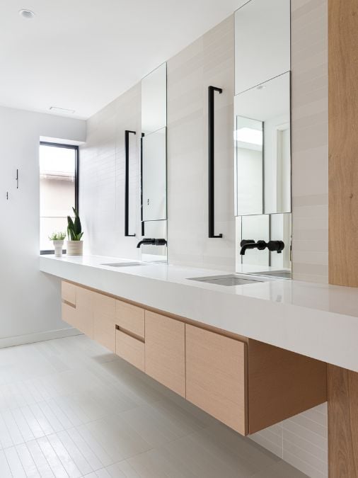 A detailed view of the bathroom, showcasing two sink stations with suspended brown cabinetry underneath, providing ample storage space.
