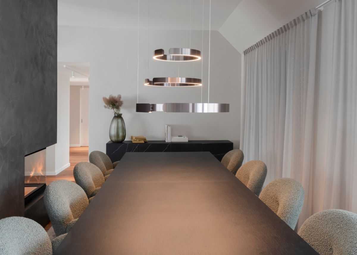 A dining room with an eight-seater long table and hand-sewn upholstery dining chairs, as well as a floor-to-ceiling open fireplace.