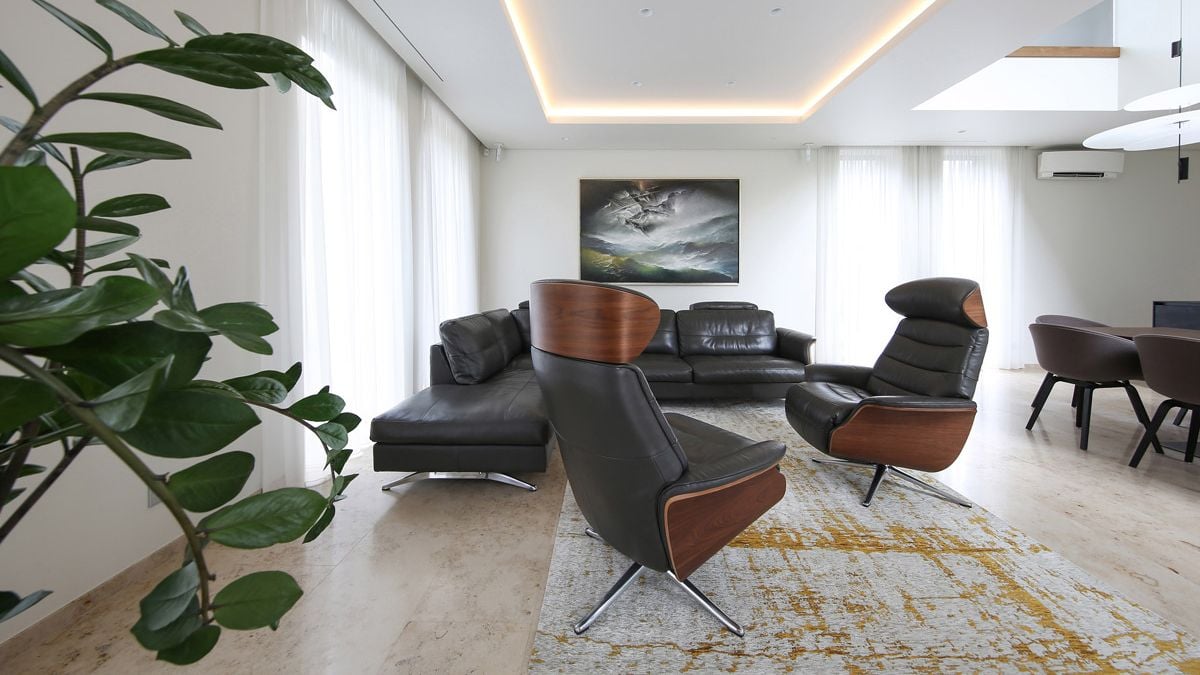 Natural Jura limestone flooring, a cozy black couch, and executive chairs with black leather complement the living room's basic white walls and curtains.