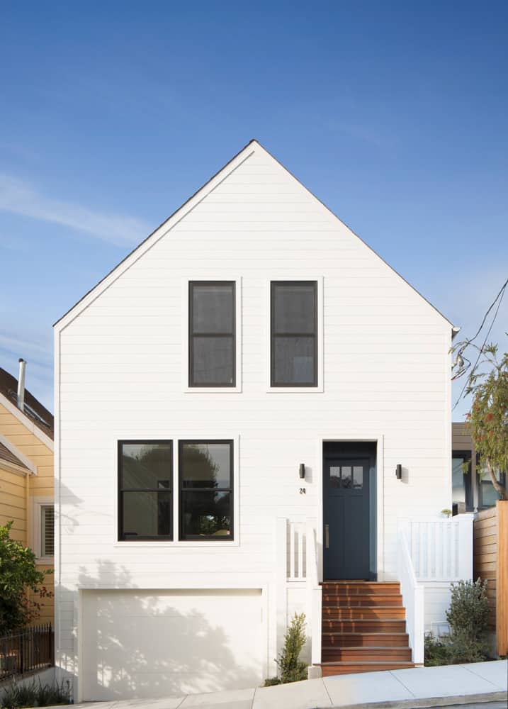 Home's facade with a sleek gable roof, stark white siding, front-loading garage, and an entry complemented with a wooden stoop.