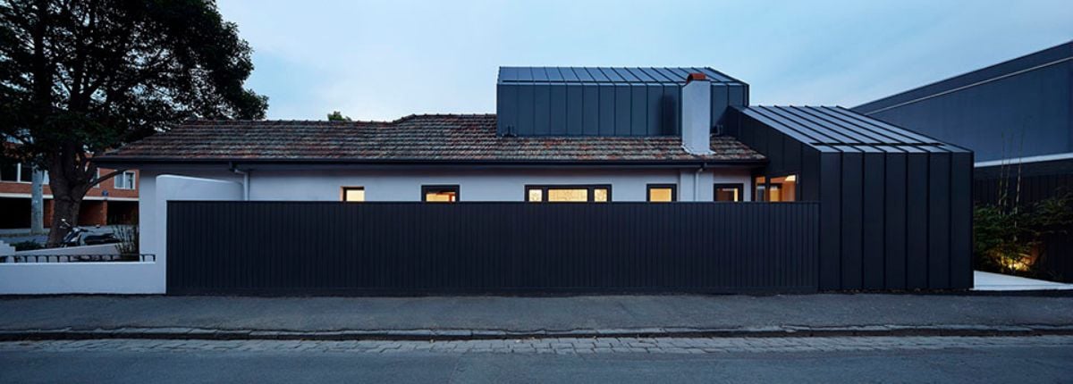 The photograph captures the exterior of the Shadow House, showcasing its new monolithic form that intentionally lacks windows facing the street to the south.