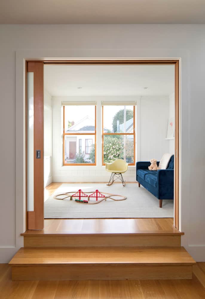 A glazed pocket door reveals the playroom with a blue couch and a small rocking chair.