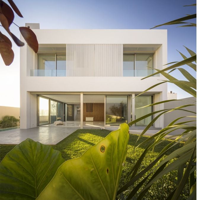An image showcasing the house's exterior design, its surrounding garden, and the large glass wall panels which provide an unobstructed view of the interior living space, seamlessly merging the indoor and outdoor environments.