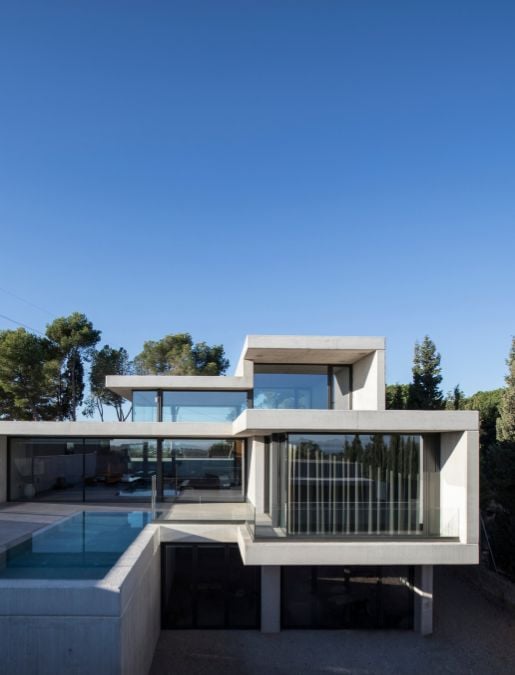 An exterior shot featuring the upper level of the building with a pool located outside, providing a panoramic view of the interior section visible through expansive glass doors and windows.