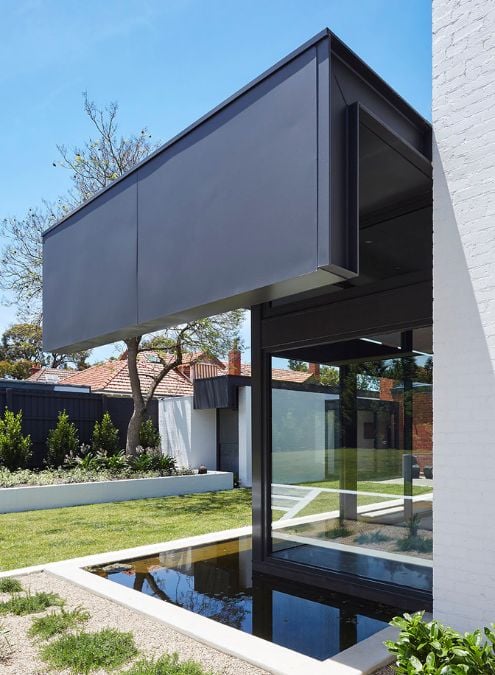 The photo provides a detailed view of a small pond in the ground, which is covered by a black cantilever roof. This structure is located outside the living room area.