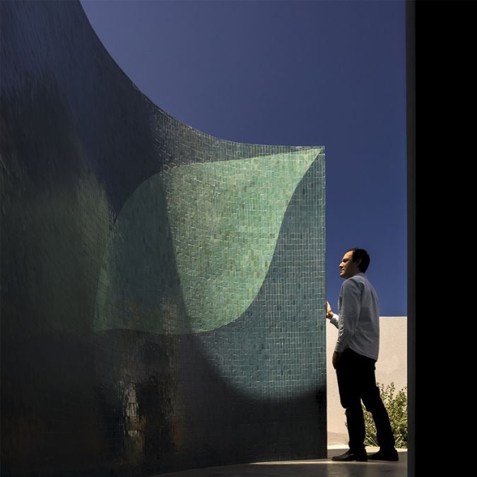 The photograph showcases a focused view of a curved wall that is decorated with traditional Moroccan tiles known as "Zellige," featuring an olive leaf drawing that serves as the inspiration for the house's name, "Villa Salam."