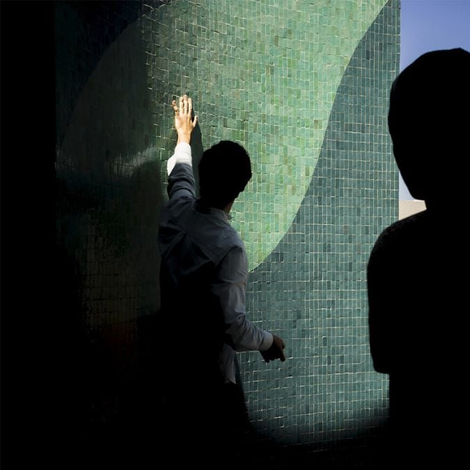 A photograph of the curved wall, featuring a man pointing to an olive leaf drawing which adds an element of interest and intrigue to the image.
