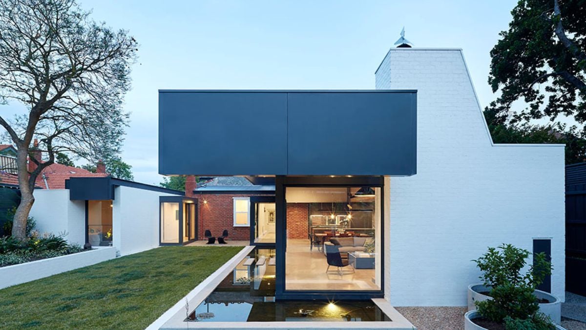 The photo captures the modern portion of the house, characterized by a prominent glass wall panel that serves as a connecting element to the old structure.