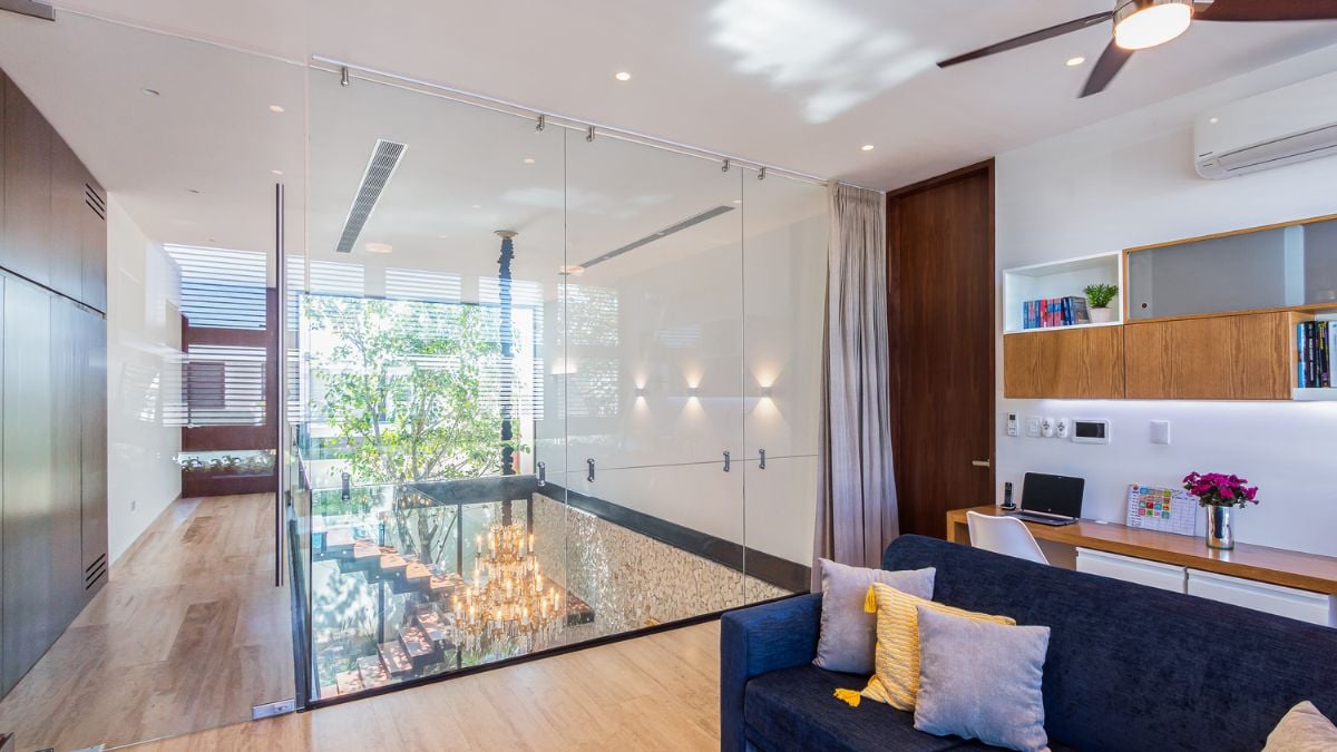 An interior shot of the upper level of a house, highlighting its interior design and frames a glimpse of the staircase visible through a glass wall panel.