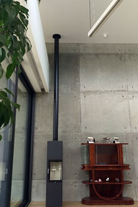 The living room features a raw concrete wall that provides a striking backdrop, accentuating the presence of a free-standing fireplace.