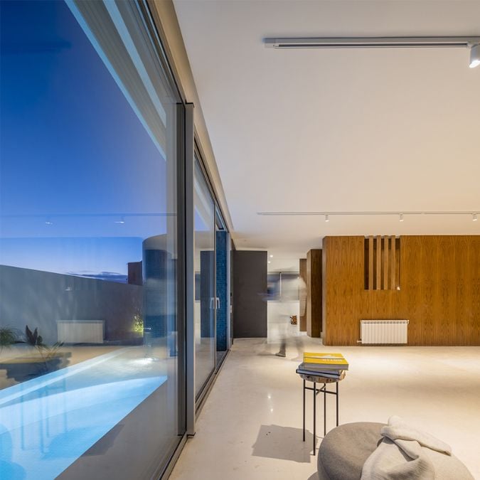 The image features a view of the living area captured from a different perspective, showcasing an expansive glass wall that provides a clear view of the pool area.