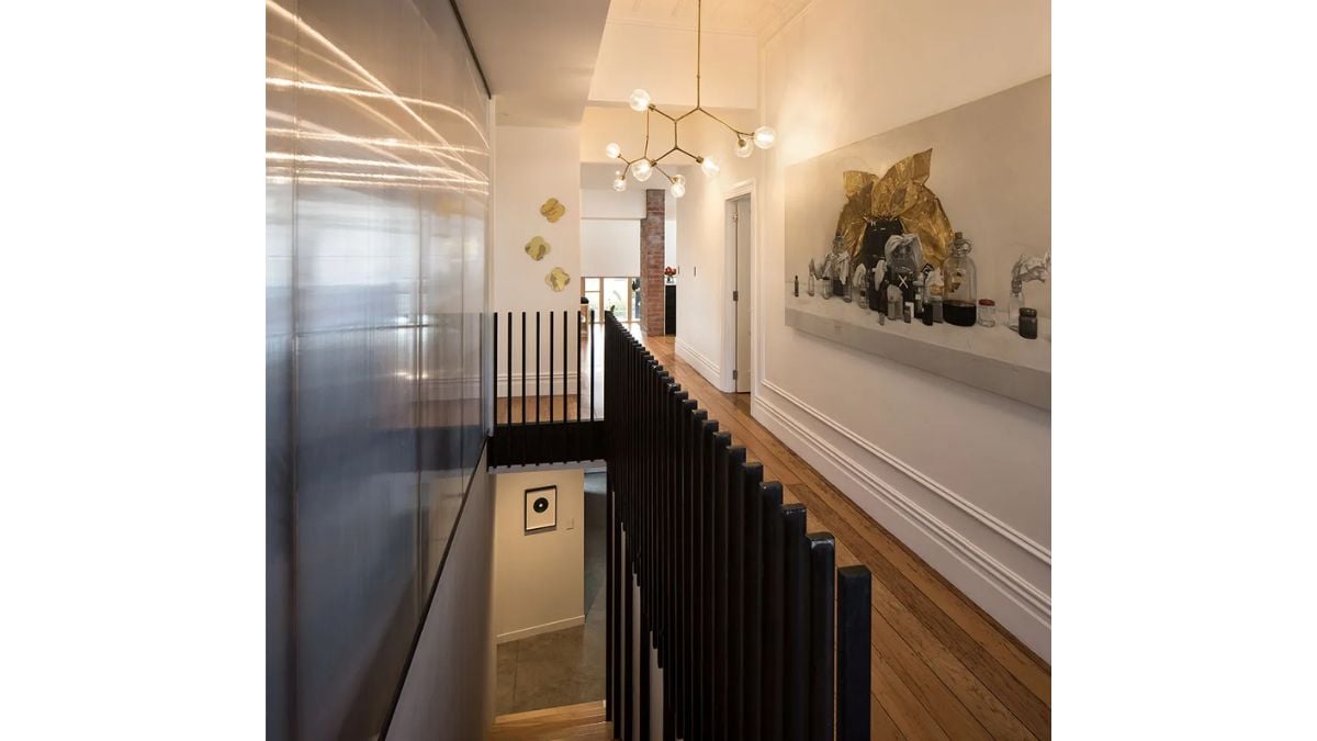 A large painting on the hallway wall, a distinctive chandelier, a wooden floor, and white painted walls make up the upper portion of the house.