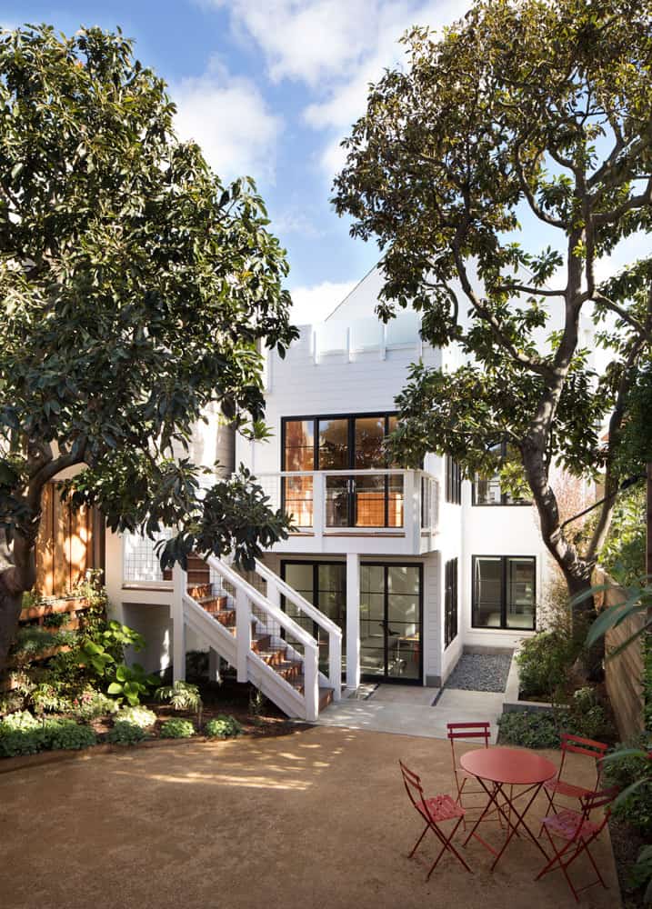View of the house from the backyard showcasing its expansive windows, second-level balcony, and an exterior staircase that leads to the private courtyard.