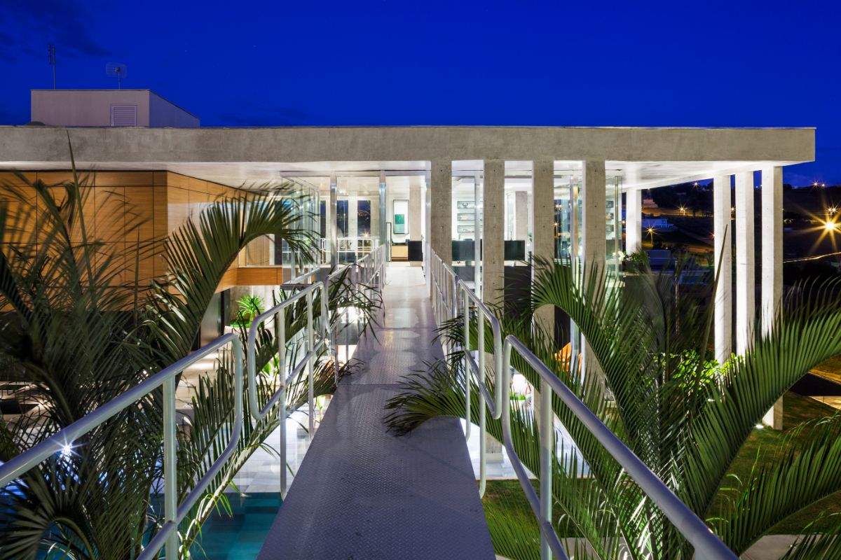 The metallic walkways connect the house to compensating slopes that occasionally form a wall, revealing a beautiful garden.