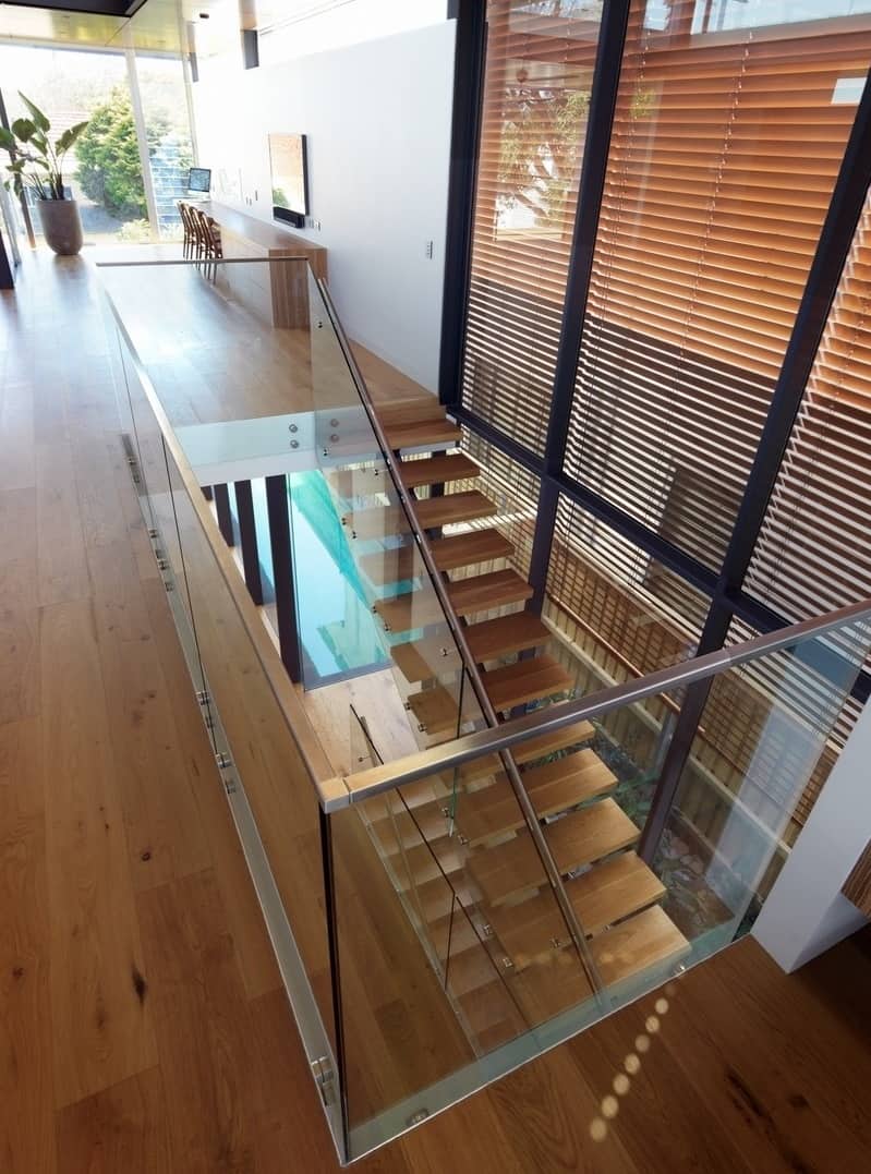 A modern staircase framed with a glass railing leads to the lower-level bedrooms.