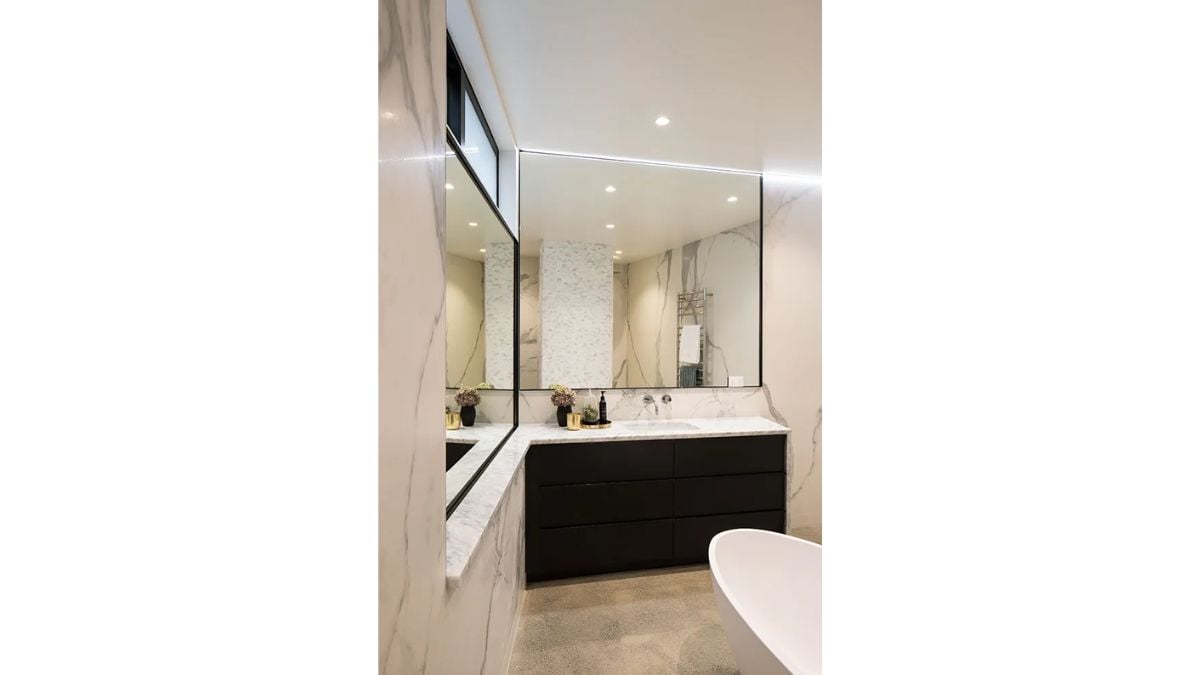 White walls with lining pattern, a white bathtub, and large mirrors can be found in the bathroom.