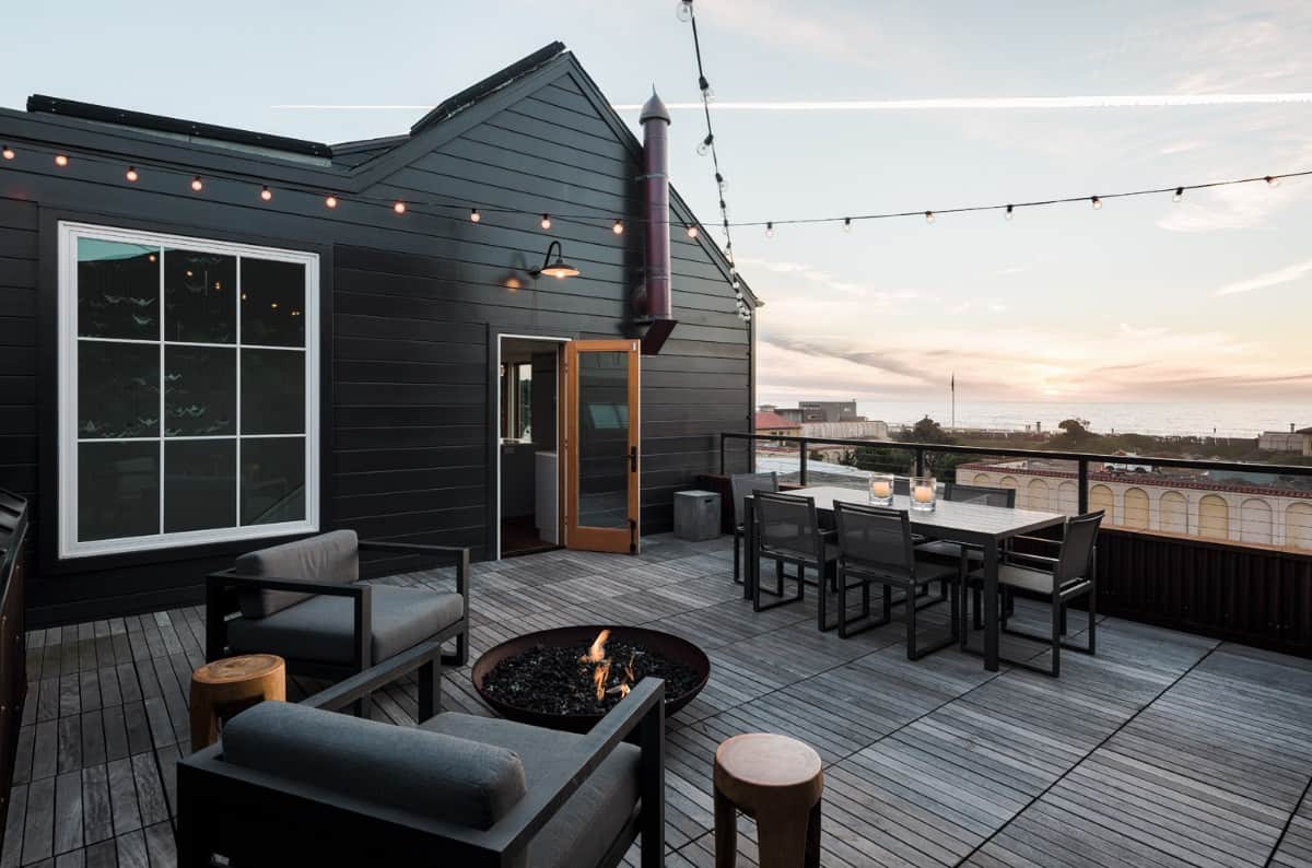 The open deck offers a fire pit sitting and outdoor dining illuminated by string lights.