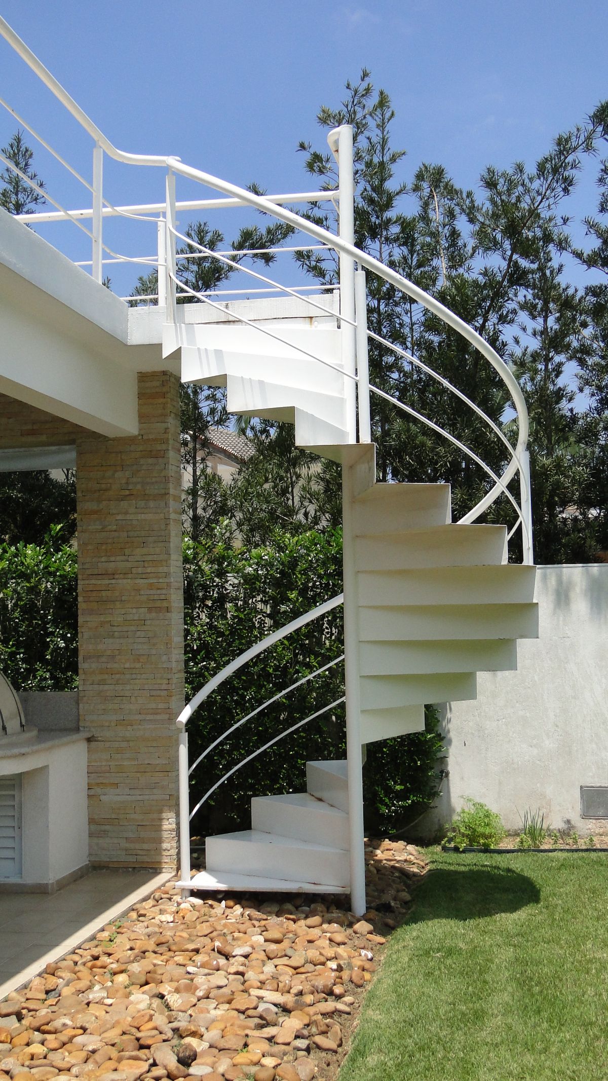 The backyard features a spiral staircase and river rocks before the lawns.