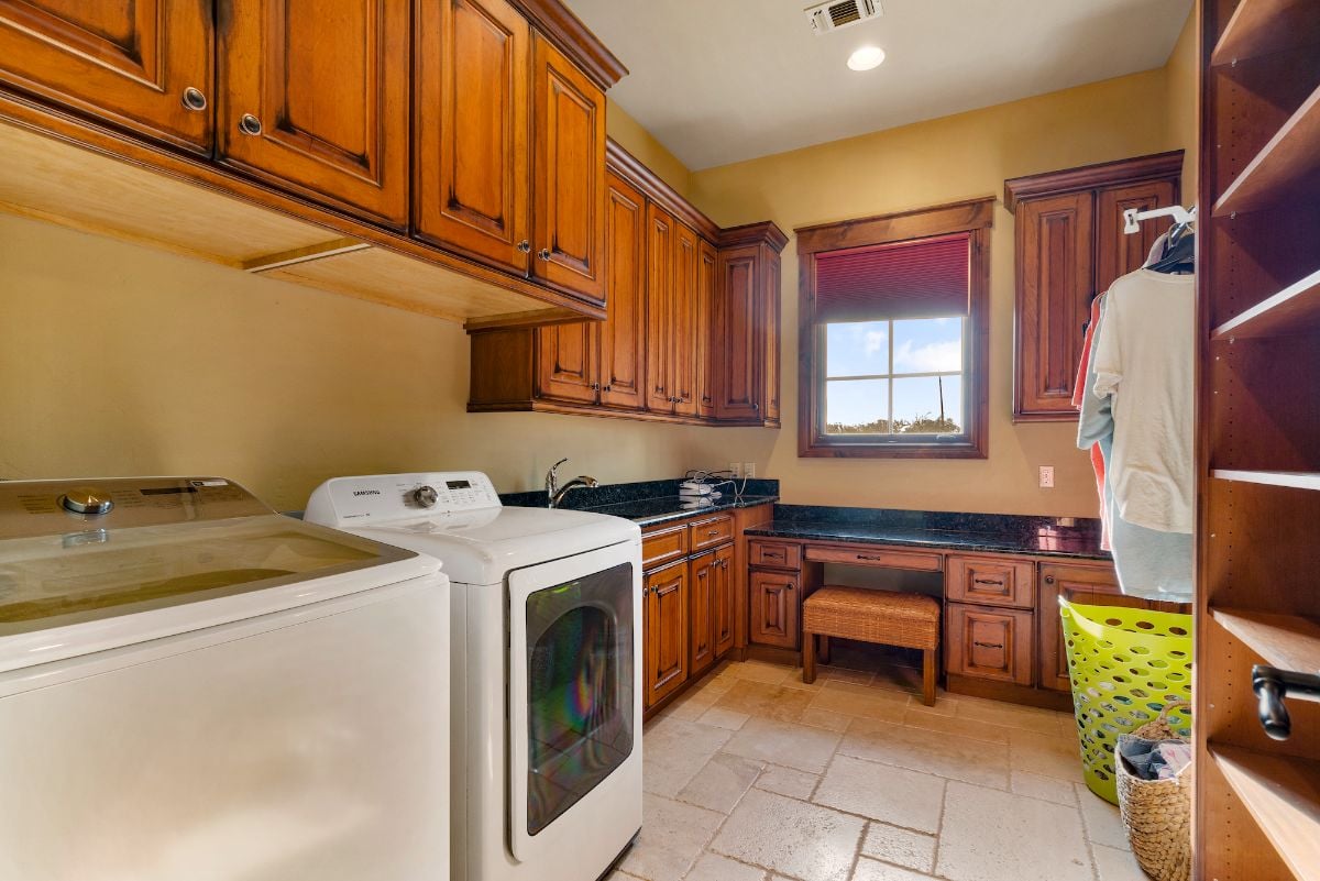 The laundry room features a wooden cabinet that blends well with the tile flooring creating a rustic feel.