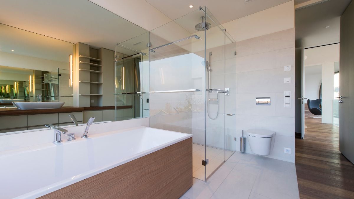 The bathroom features a huge bathtub, a mirror, glass shower doors, and a white toilet next to a white wall.
