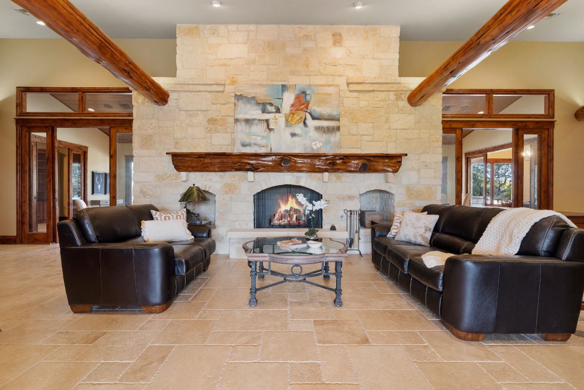 The fireplace area features leather sofas, and the wooden beams give the room a rustic feel.