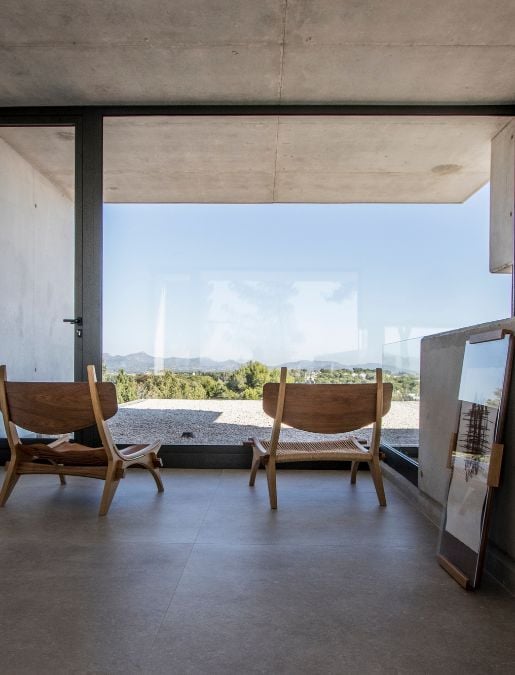 A photograph captures from the bedroom featuring the expansive view of nature through the large glass panels.