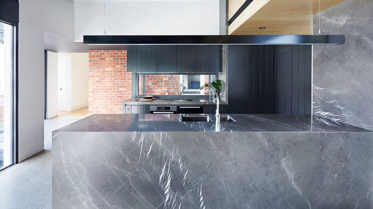 This detailed photograph showcases the kitchen area, with a large center island made of black marble and a red brick wall located near the stove.