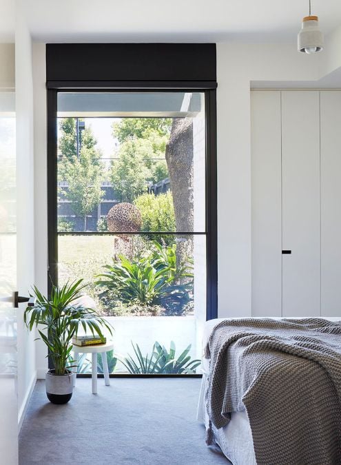 Photograph taken inside a bedroom, highlighting a full-height glass window that allows natural light to enter the room.