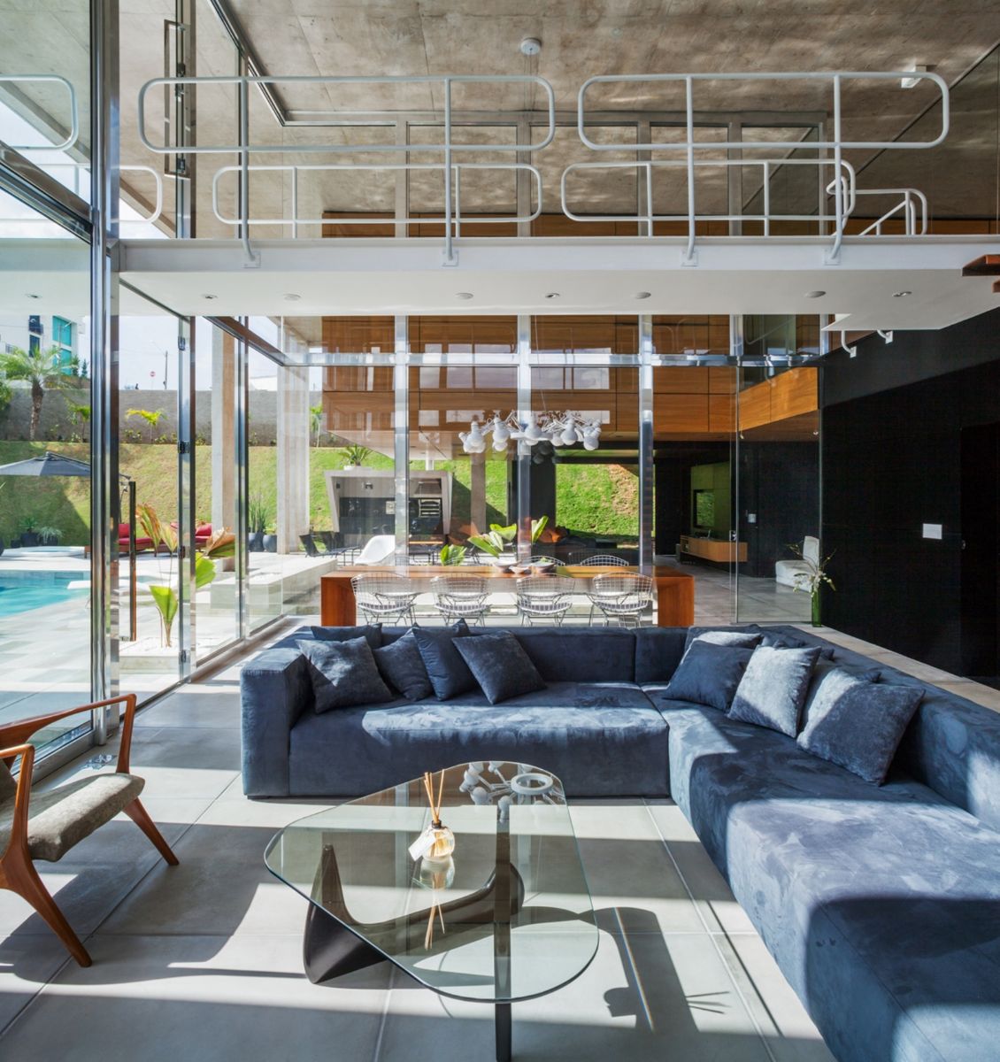 A bright and airy double-height living room with cushioned sofas and a glass-topped center table.