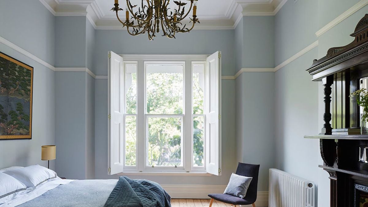 An interior photograph of a bedroom with a light blue wall color, creating a cool and vibrant ambiance. The room also features vertical folding windows.