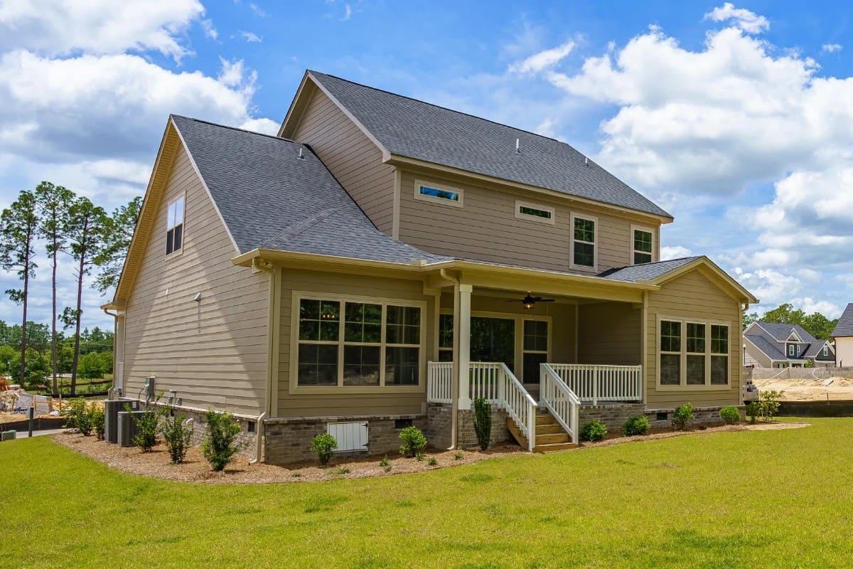 Rear-right exterior view with horizontal lap siding, brick skirting, and a covered porch bordered with white railings.